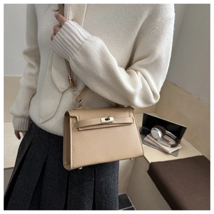 Detailed side view of khaki pebbled leather handbag with adjustable strap on a wooden desk