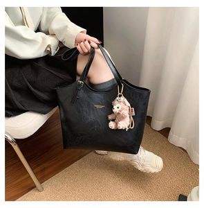 Detail of black leather tote bag with gold lettering and a pink plush bear charm