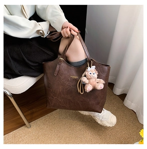Detail of a brown leather tote with vintage texture and adjustable strap and plush charm