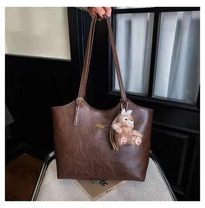 Detail view of brown leather tote bag with plush bunny pendant on a white chair