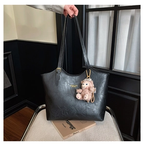 Detail of black faux leather tote with golden buckle straps and pink plush pendant