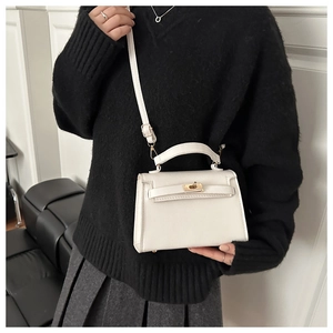 Detail of white lychee leather texture and gold metal twist lock on a handheld tote bag