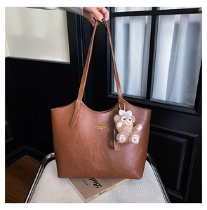 Macro shot of brown retro leather tote bag featuring golden lettering and plush bear charm