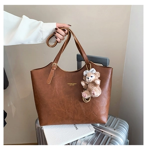 Detail of brown leather tote bag with gold lettering and plush character charm accessory