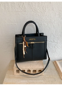 Macro detail of black litchi texture handbag with gold logo and wooden bead charm