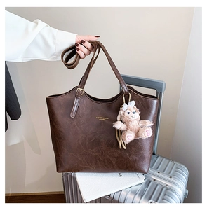Detail of vintage brown leather tote bag with gold lettering and plush bear charm