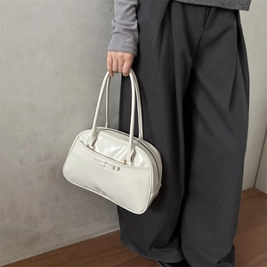 Glossy cream faux leather handbag with bow detail and twin handles shown by model