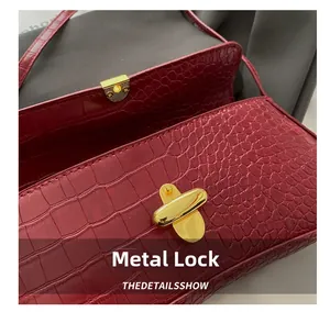 Close-up of golden metal lock and crocodile embossed leather texture on red handbag
