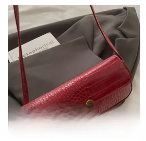Detail view of red crocodile embossed shoulder bag with gold metal twist lock and strap
