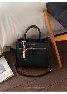 Detail of retro black faux-crocodile leather handbag with gold logo and wooden bead charm