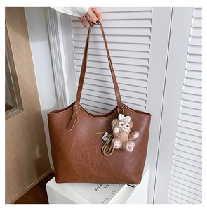 Detail of dark brown faux leather tote with golden logo and cute bear pendant charm