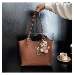 Detail of vintage brown leather tote bag featuring brand logo and plush bear charm