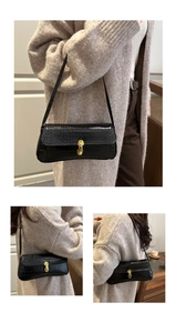 Detail of black crocodile texture baguette bag with golden U-shaped metal lock and slim strap
