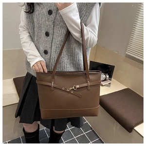 Detail of brown leather tote bag with lychee texture and gold buckle on shoulder strap