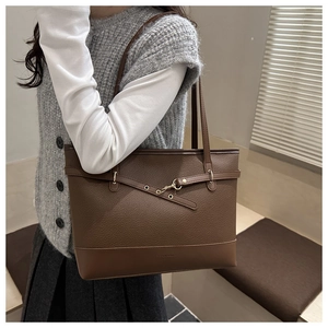 Close-up of the textured lychee leather and gold metal buckle on a brown tote bag