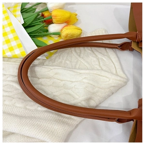 Detail of round stitched brown leather handles on a stylish tote bag with soft lighting