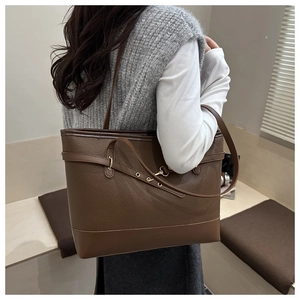 Close-up of brown textured leather tote bag with thin shoulder straps and gold hardware