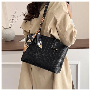 Detail of black tote bag with croc-embossed texture and decorative silk scarf on handle