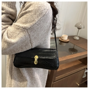 Detail of black crocodile texture baguette bag with golden metal buckle and long strap