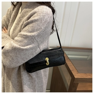 Detail of black crocodile texture baguette bag with elegant golden metal turn-lock buckle