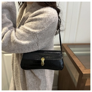 Detail of black crocodile texture baguette bag with golden U-shaped buckle on a shoulder