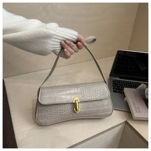 Close-up of beige crocodile pattern handbag featuring a gold twist-lock and shoulder strap