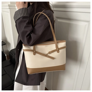 Detail of color-block tote bag featuring beige lychee leather and brown strap accents