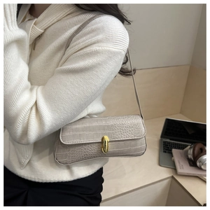 Chic beige crocodile texture baguette bag with golden clasp shown on shoulder
