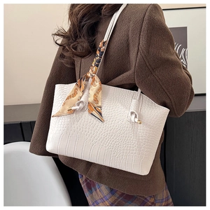 Detail of white faux crocodile tote bag with a decorative silk scarf on the handle