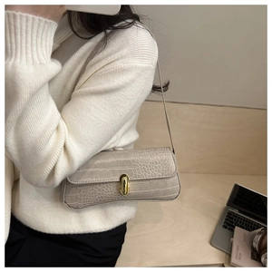 Close-up of minimalist beige shoulder bag featuring crocodile texture and golden oval lock