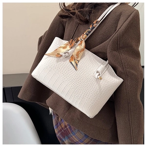 Detail of white crocodile embossed tote bag featuring elegant decorative handle silk scarf