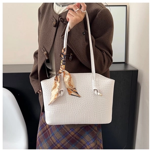 Detail of white crocodile texture tote bag with elegant orange silk scarf on the handle