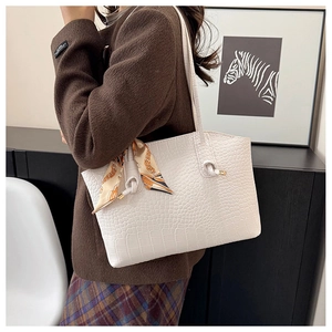 Detail of beige crocodile embossed tote bag featuring an orange silk scarf on the strap