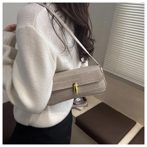 Close-up of beige crocodile texture handbag with gold clasp on model shoulder
