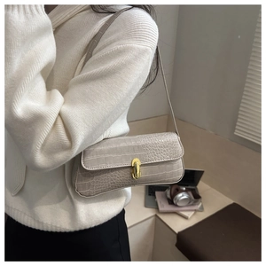Detail of a beige crocodile pattern baguette bag with a gold metal clasp worn by a model