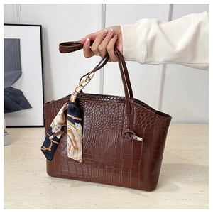 Macro detail of brown crocodile embossed tote bag with elegant floral scarf on handle