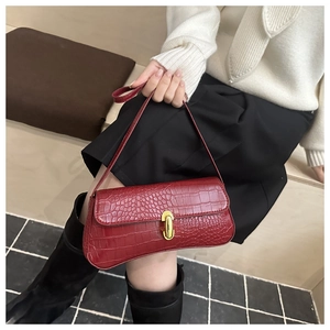Detailed shot of red crocodile pattern handbag with gold clasp on model shoulder