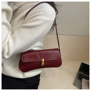 Detail of dark red crocodile embossed baguette bag with golden buckle and strap