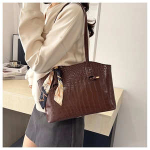 Detail of dark brown faux crocodile leather tote bag with a decorative silk scarf on handle