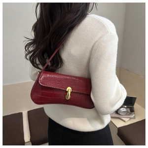 Detail of dark red crocodile pattern baguette bag with a stylish gold metal clasp