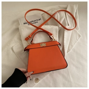 Detail view of the orange leather handbag featuring a square metal twist lock and stitching