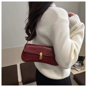 Detail of dark red crocodile pattern baguette bag with a gold lock on a white sweater