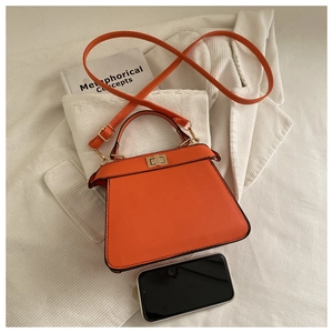 Detail of orange trapezoid handbag with gold twist lock and adjustable shoulder strap