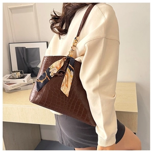 Detail of dark brown croc-effect tote bag with silk scarf on model in chic interior