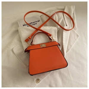 Macro view of bright orange leather handbag with golden metal twist lock on white fabric