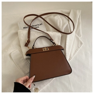 Detail view of brown trapezoid handbag with gold metal twist lock and adjustable strap