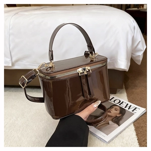 Detail of a deep brown patent leather box bag with gold metal hardware and a top handle