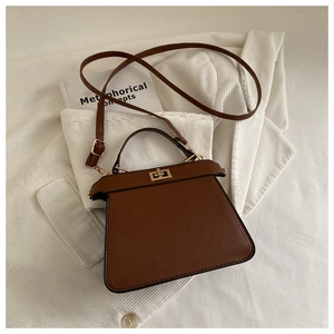 Brown trapezoid handbag with metal twist lock displayed on a minimalist background