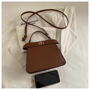 Détail d'un sac à main trapèze en cuir marron avec fermoir tournant en métal et poignée élégante