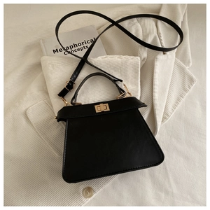 Black trapezoid handbag with gold twist lock and adjustable strap on a book